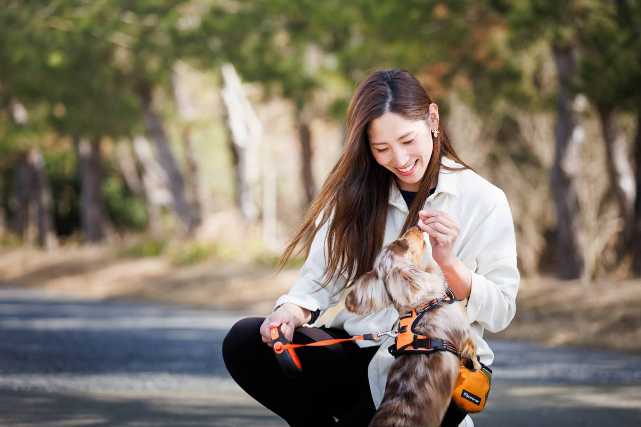 屋外で女性が犬と向き合い、ご褒美を与える様子